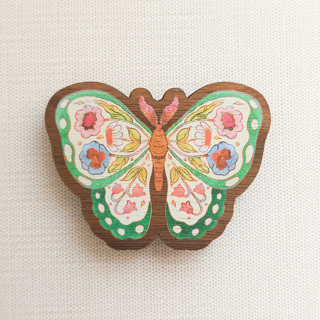 wooden magnet with an illustration of a green butterfly with flowers in its wings on a linen background