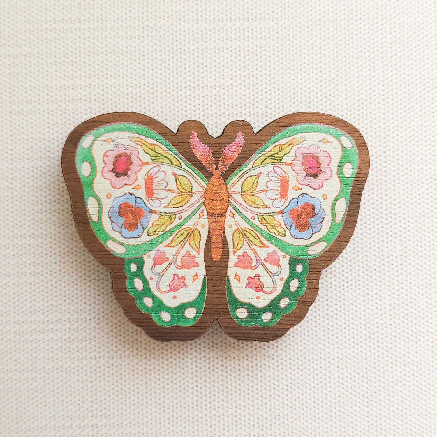 wooden magnet with an illustration of a green butterfly with flowers in its wings on a linen background
