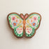 wooden magnet with an illustration of a green butterfly with flowers in its wings on a linen background