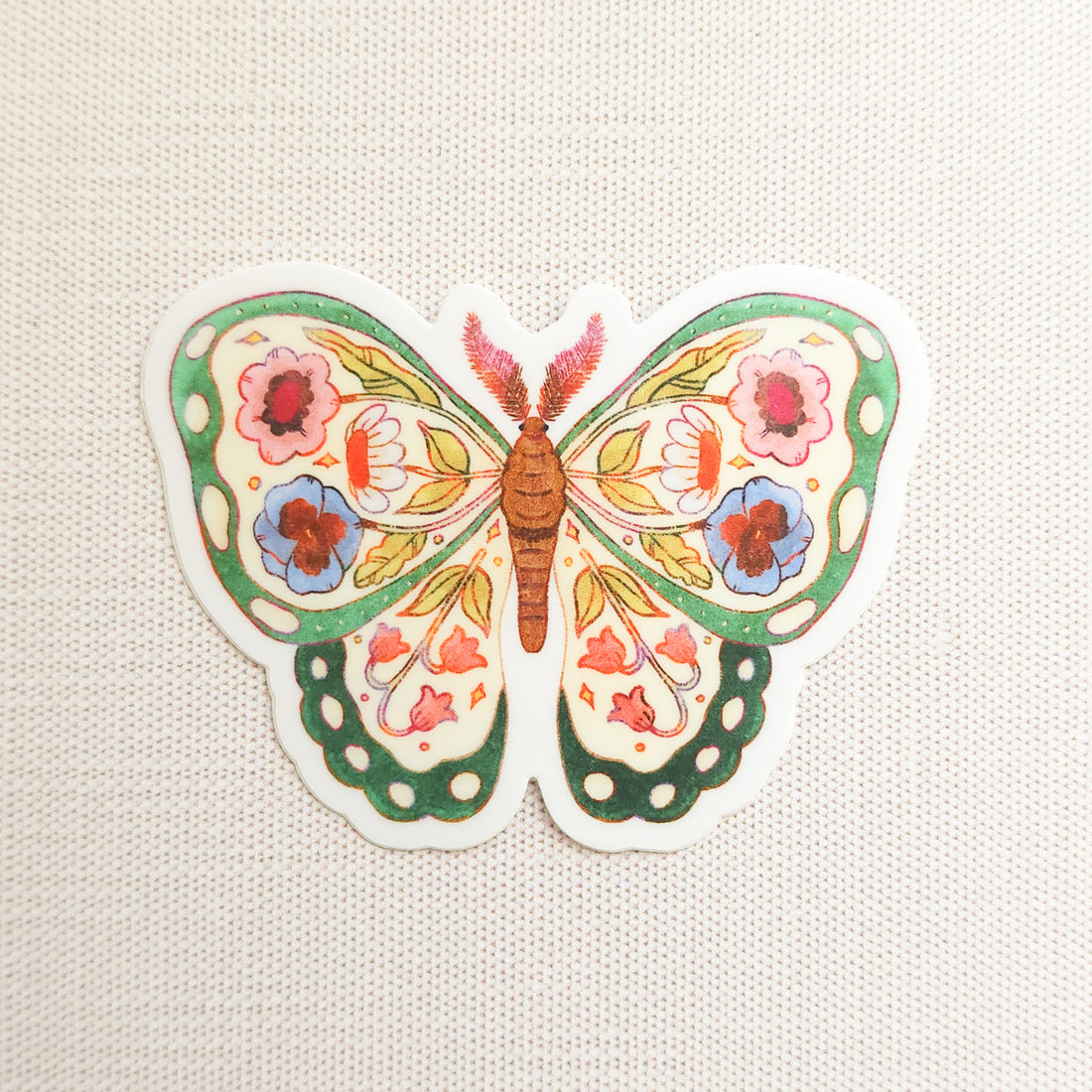 sticker of an illustrated green butterfly with flowers in its wings on a linen background