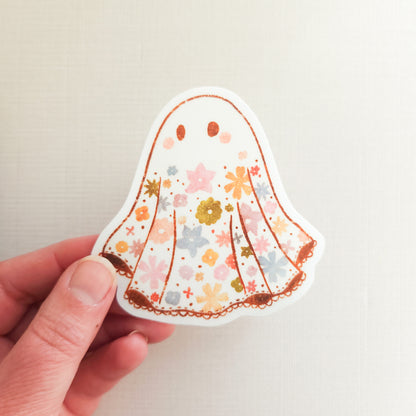 Hand holding a floral-patterned ghost sticker against a plain background