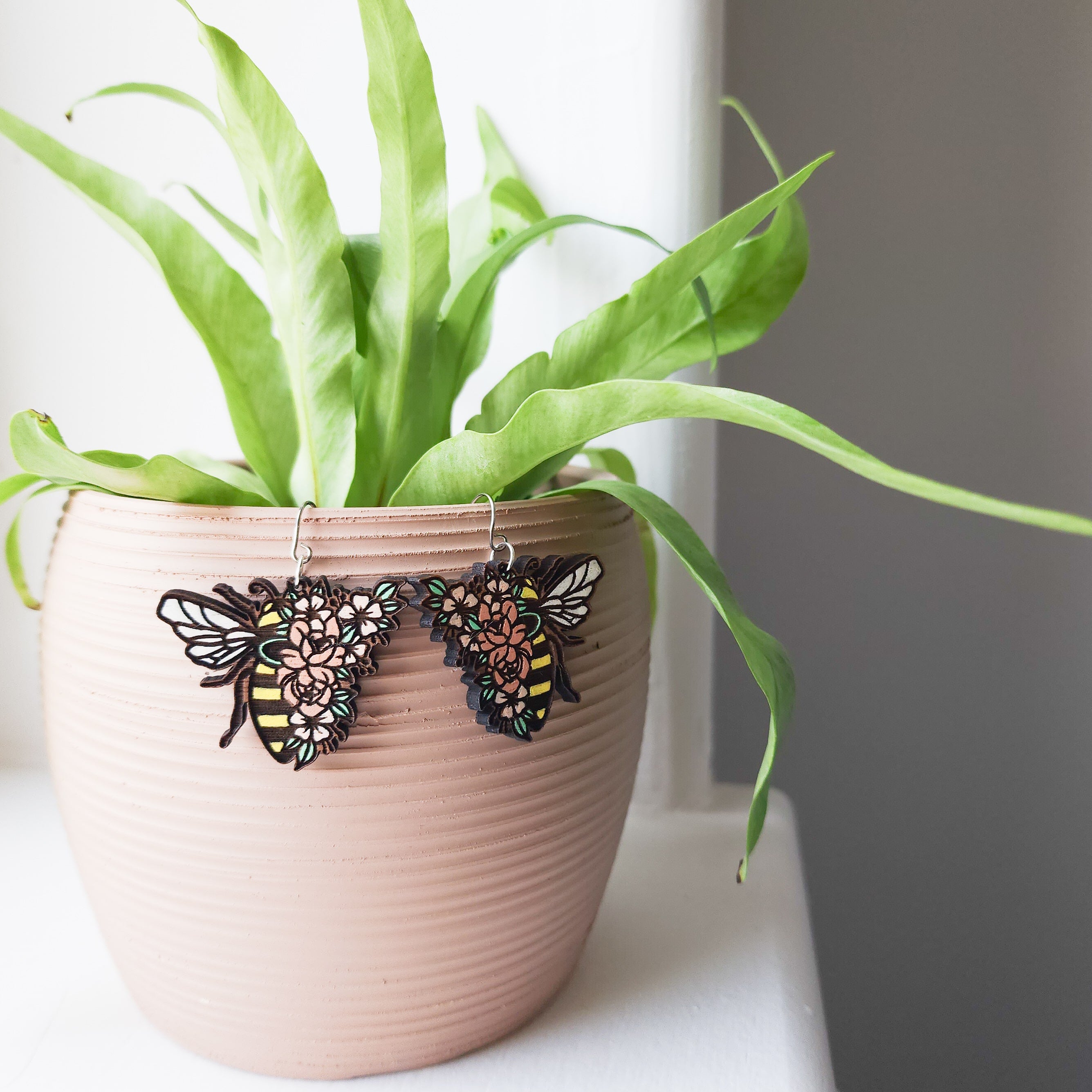 floral bee earrings hanging off a plant pot