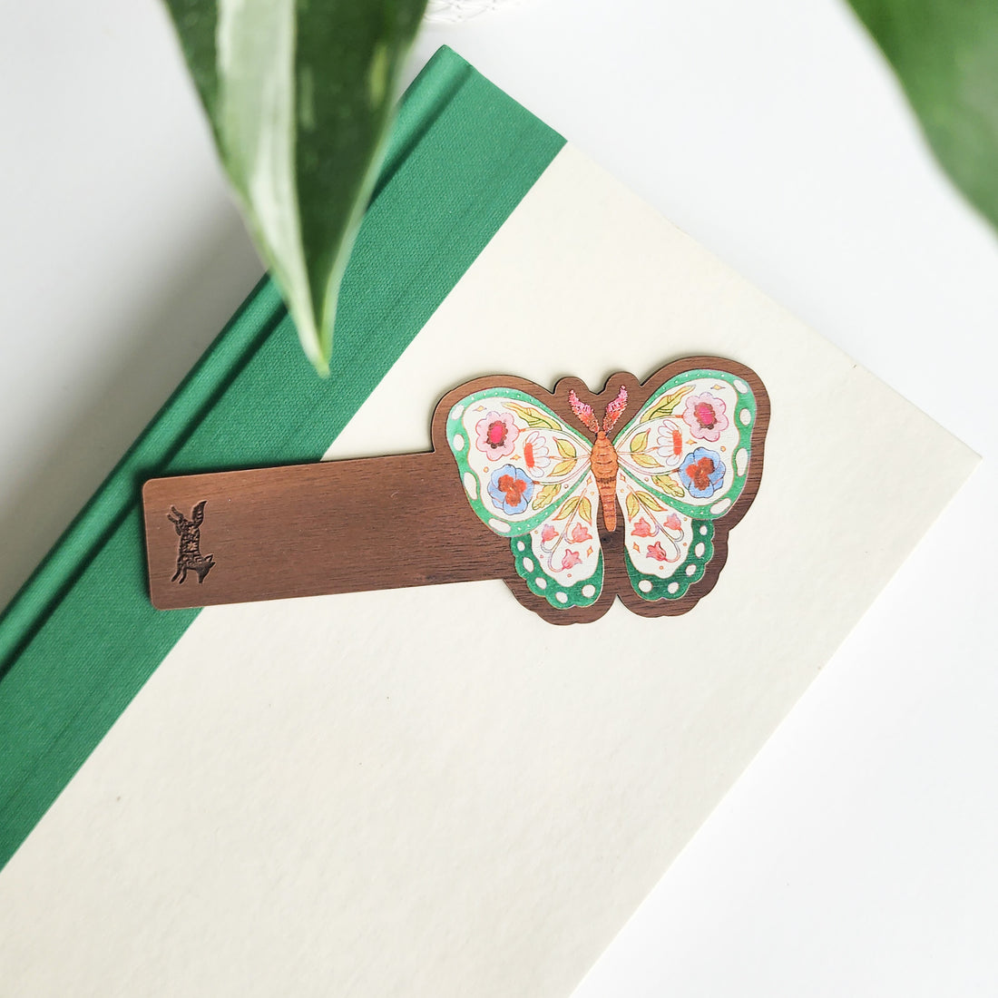 Butterfly-shaped wooden bookmark on a green book with leaves in the background