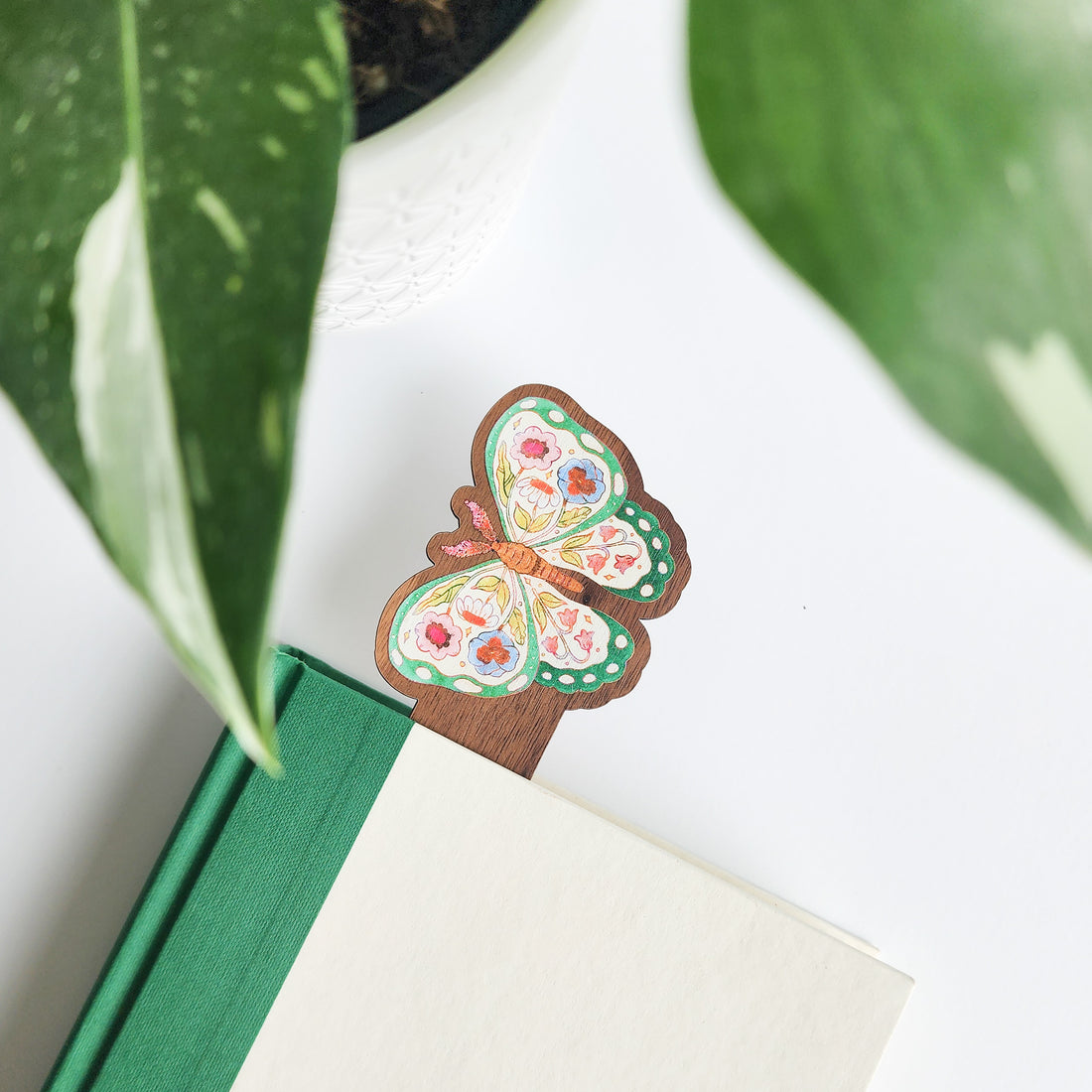 Butterfly-shaped wooden bookmark inside a green book with leaves in the background