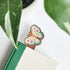 Butterfly-shaped wooden bookmark inside a green book with leaves in the background