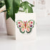 Card with a colorful butterfly design on a white surface with a plant in the background