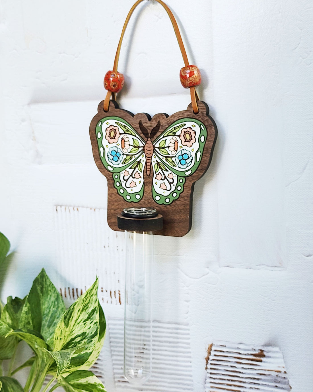 propagation station with a butterfly with flowers in its wings painted on it, hanging on a white wall