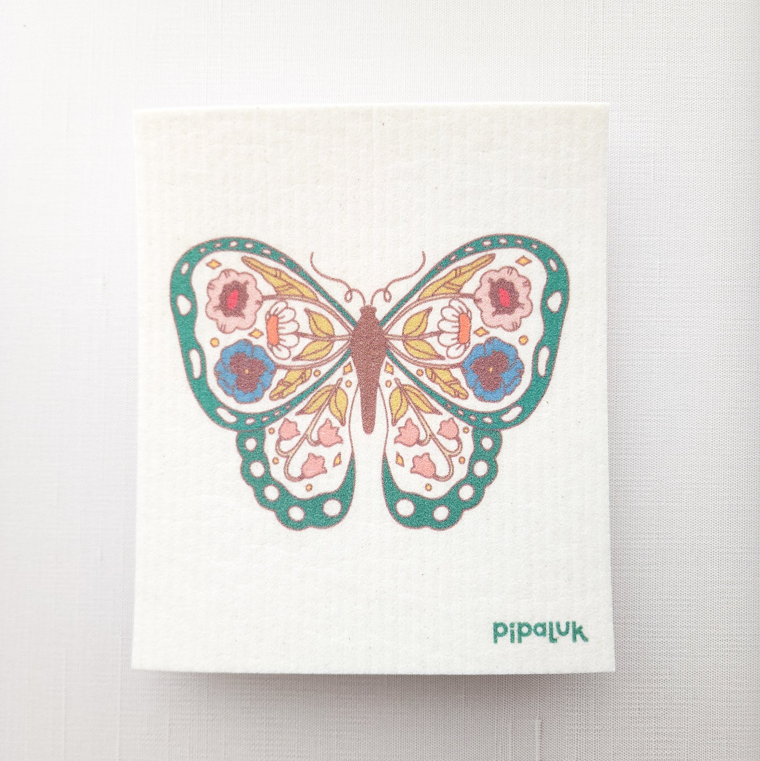 swedish dishcloth on a white background with a green floral butterfly design printed on it and a Pipaluk logo in the bottom right corner