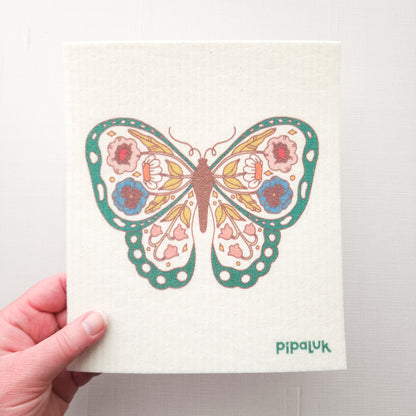 swedish dishcloth with a green, floral, butterfly design held in a hand on a white background