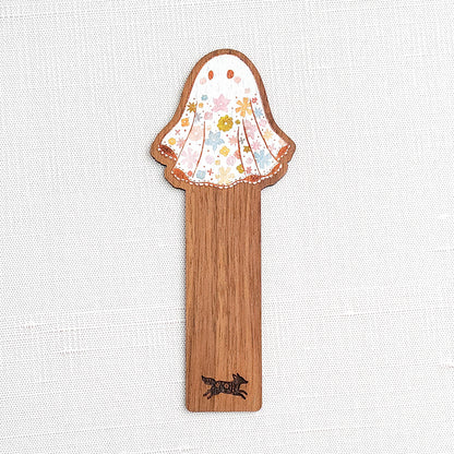 Wooden bookmark featuring a little floral ghost with colorful flowers and stars on its sheet, printed on walnut wood and photographed on a neutral fabric background.