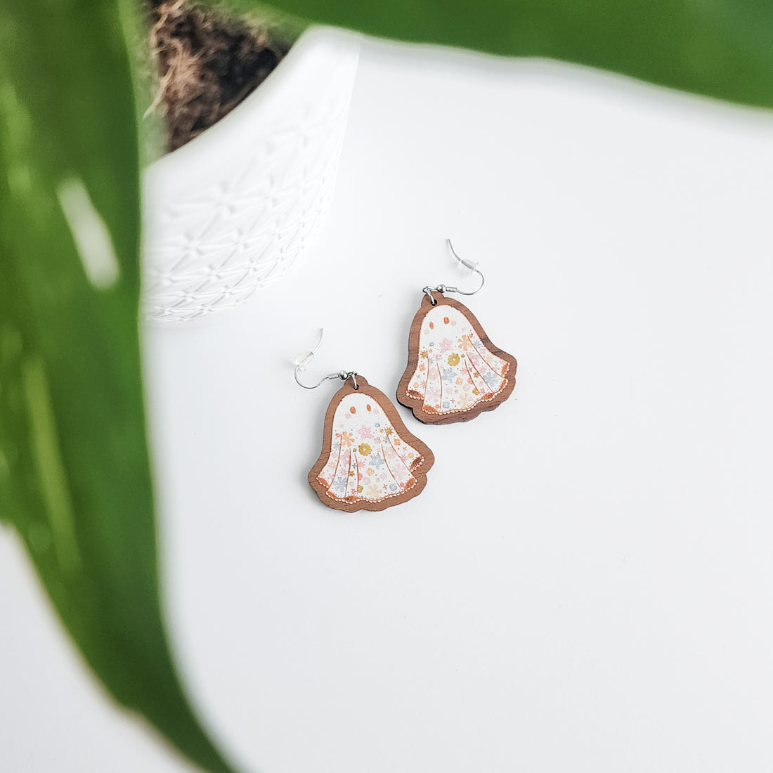 floral ghost earrings on a white background with a potted plant