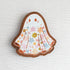 Wooden magnet featuring a little floral ghost with colorful flowers and stars on its sheet, printed on walnut wood and photographed on a neutral fabric background.