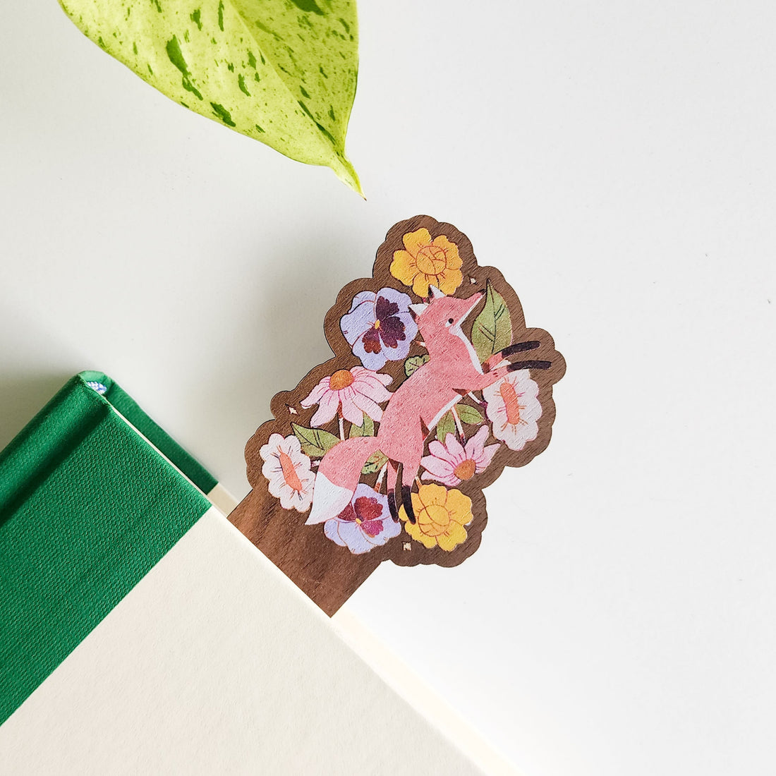 wood bookmark with an image of a fox leaping through flowers tucked in a book
