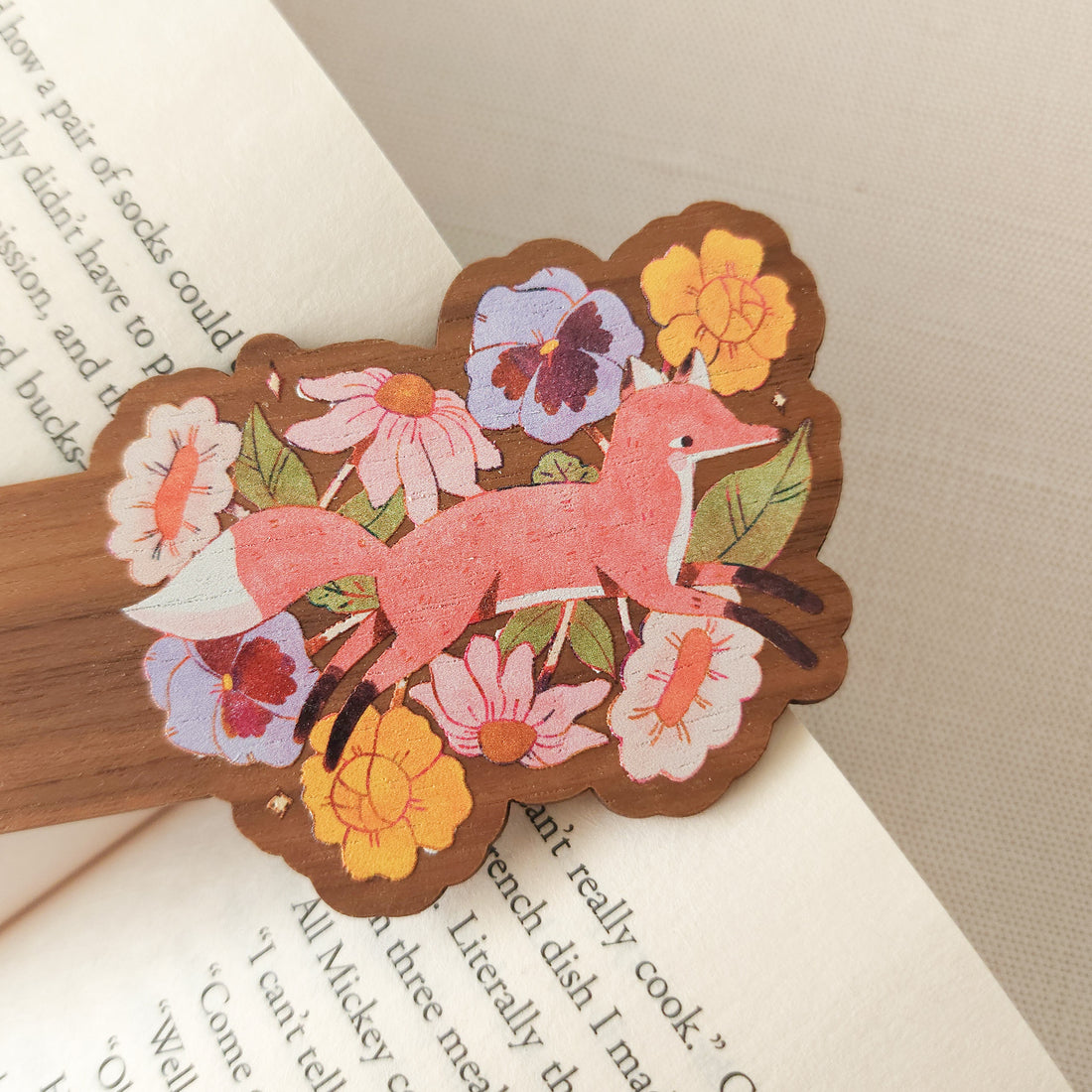 wooden bookmark with a floral fox illustration sitting on an open book