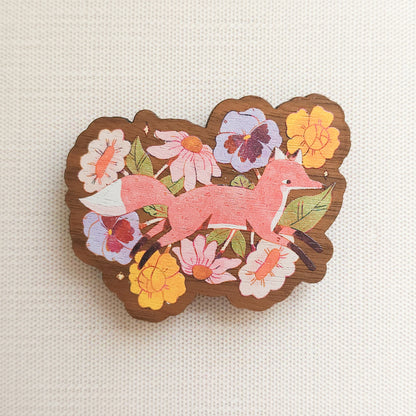 wooden magnet with an illustration of a fox jumping through flowers on a linen background