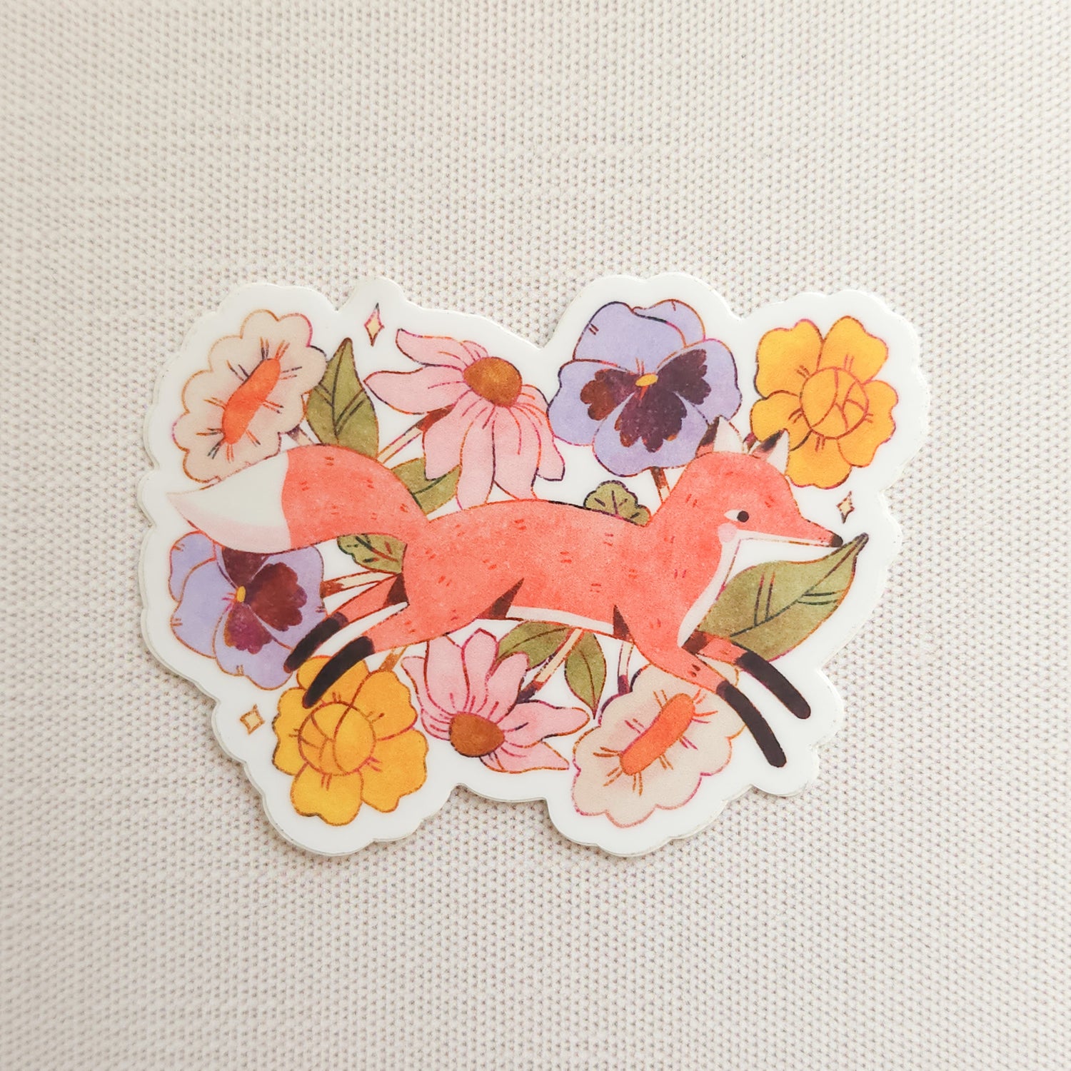sticker with an illustration of a fox jumping through flowers on a linen background