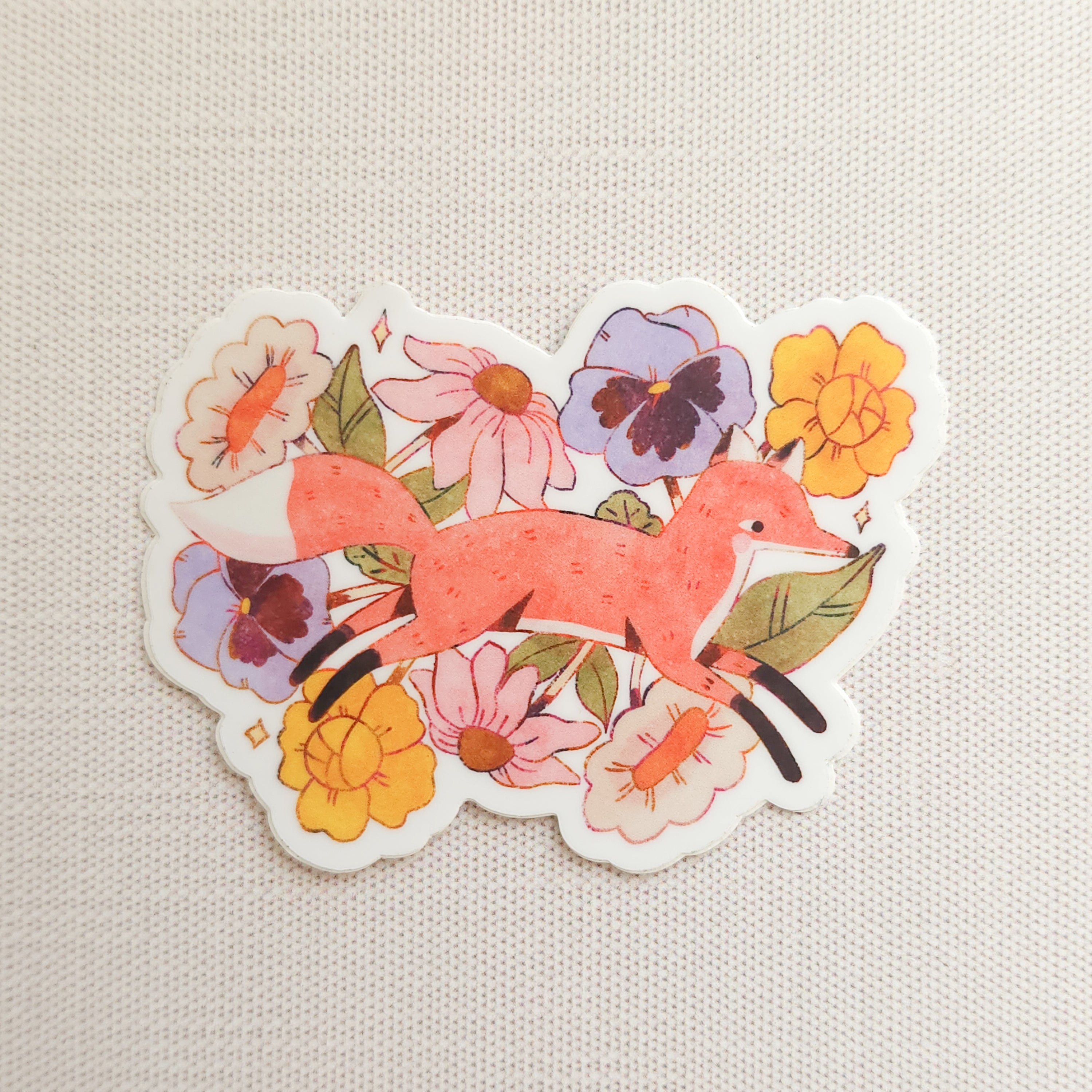 sticker with an illustration of a fox jumping through flowers on a linen background