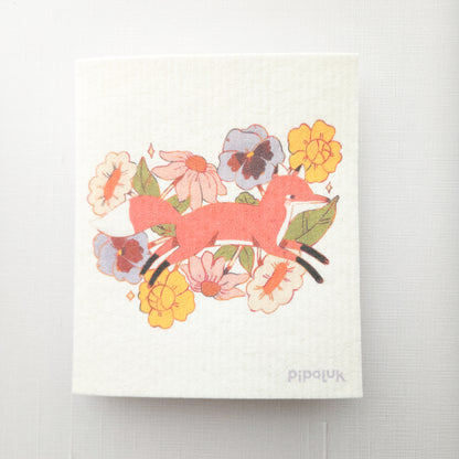 swedish dishcloth with an illustration of a fox jumping through flowers and a pipaluk logo in the bottom corner on a white background