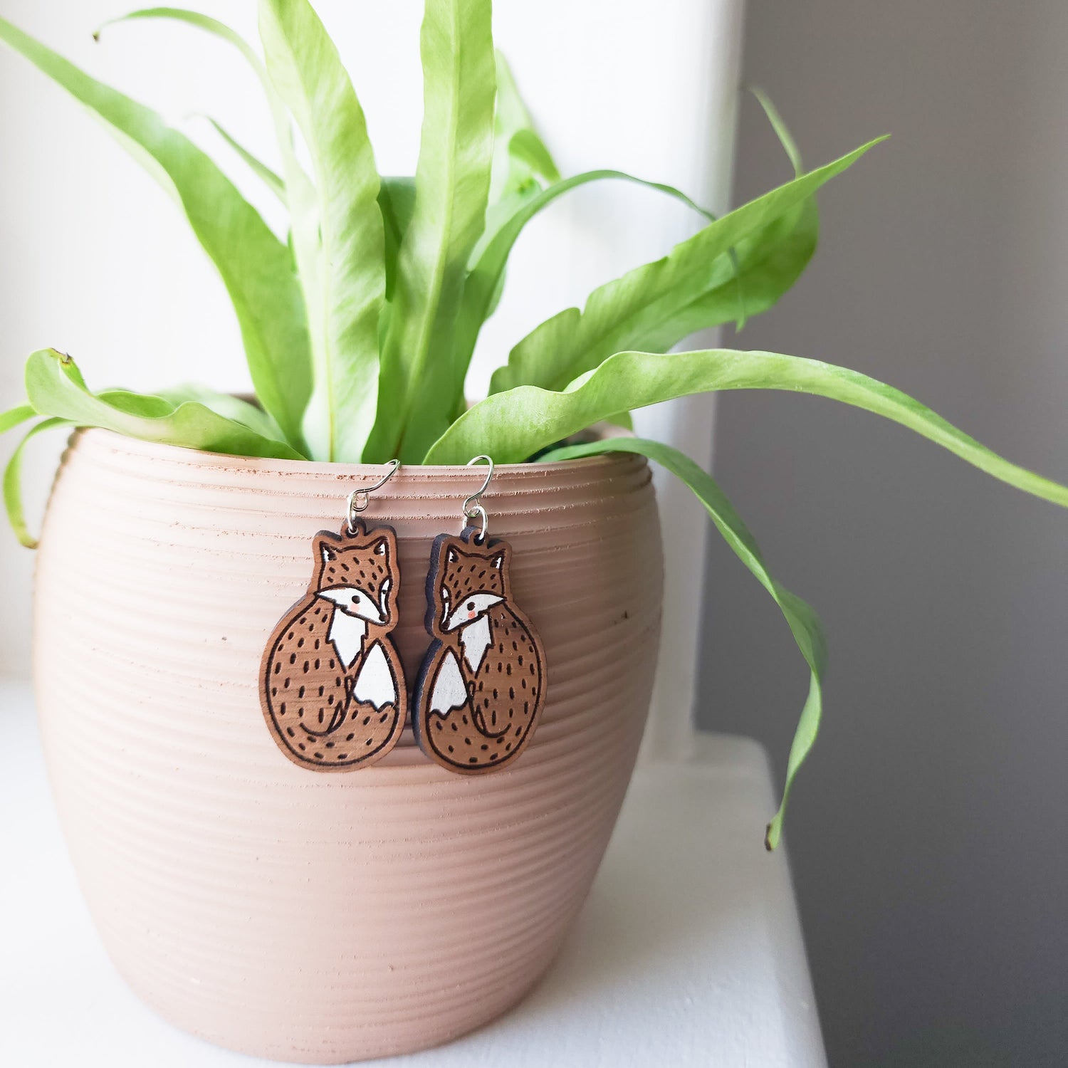 fox dangle earrings hanging off of a potted plant