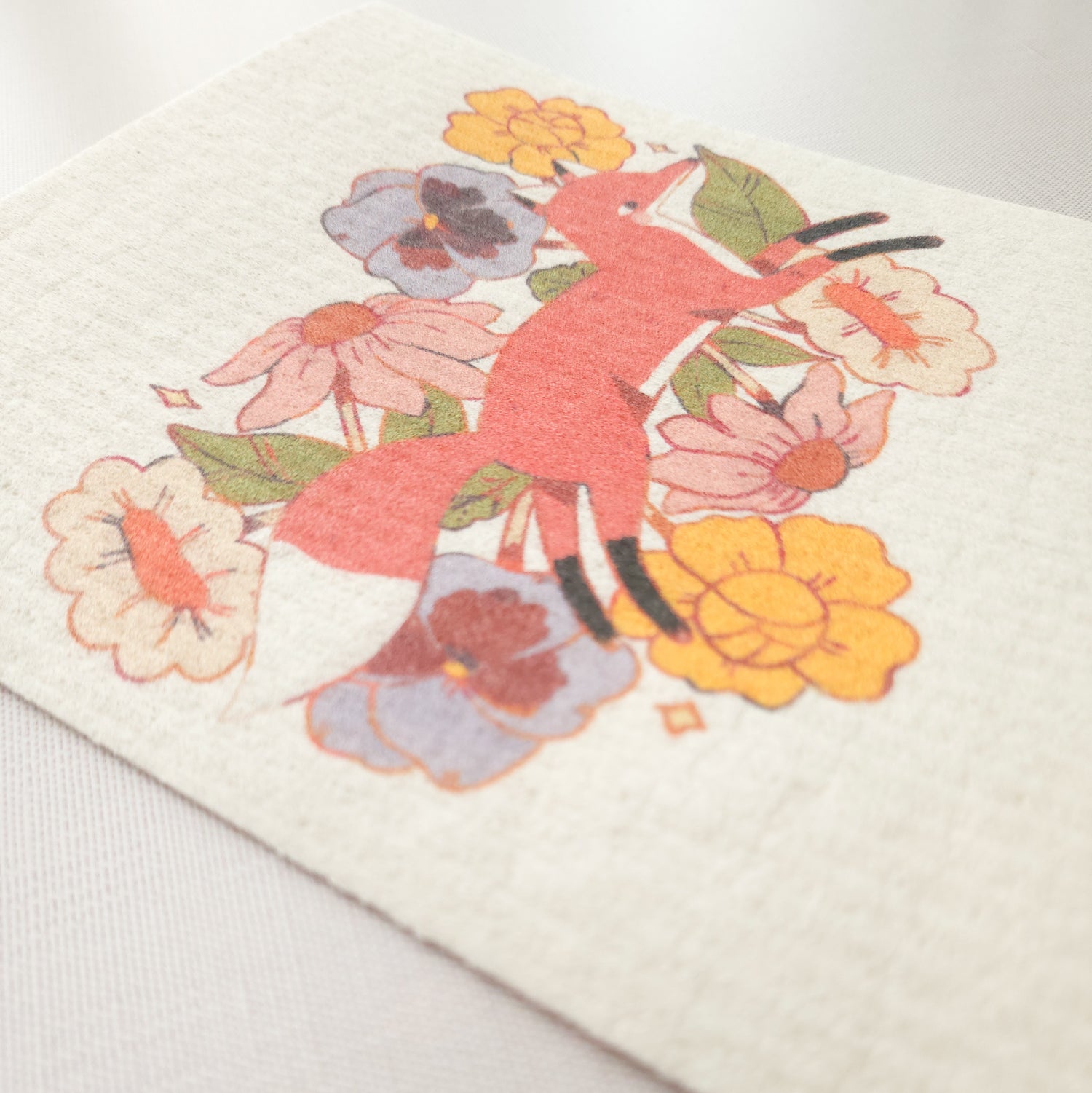close up image of a swedish dishcloth an illustration of a fox jumping through flowers, showing the texture of the cloth