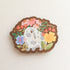 wooden magnet with an illustration of a gray and white bunny surrounded by flowers on a linen background