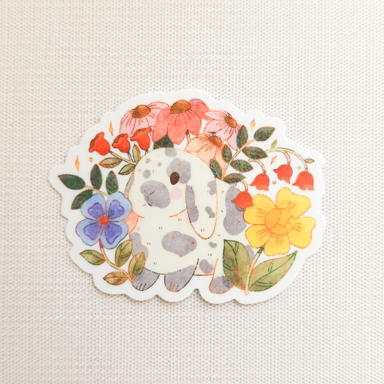 sticker with an illustration of a gray and white bunny surrounded by flowers on a linen background