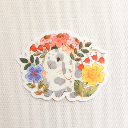 sticker with an illustration of a gray and white bunny surrounded by flowers on a linen background