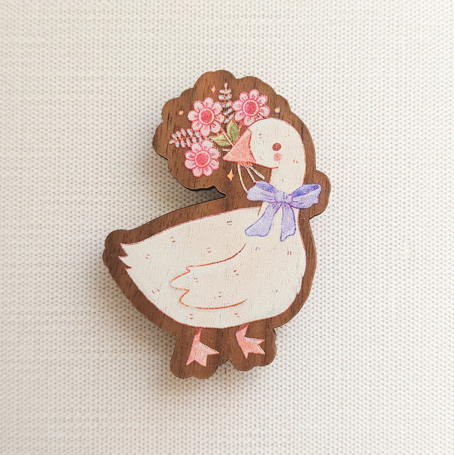 wooden magnet with an illustration of a goose holding a bouquet of flowers in its beak on a linen background
