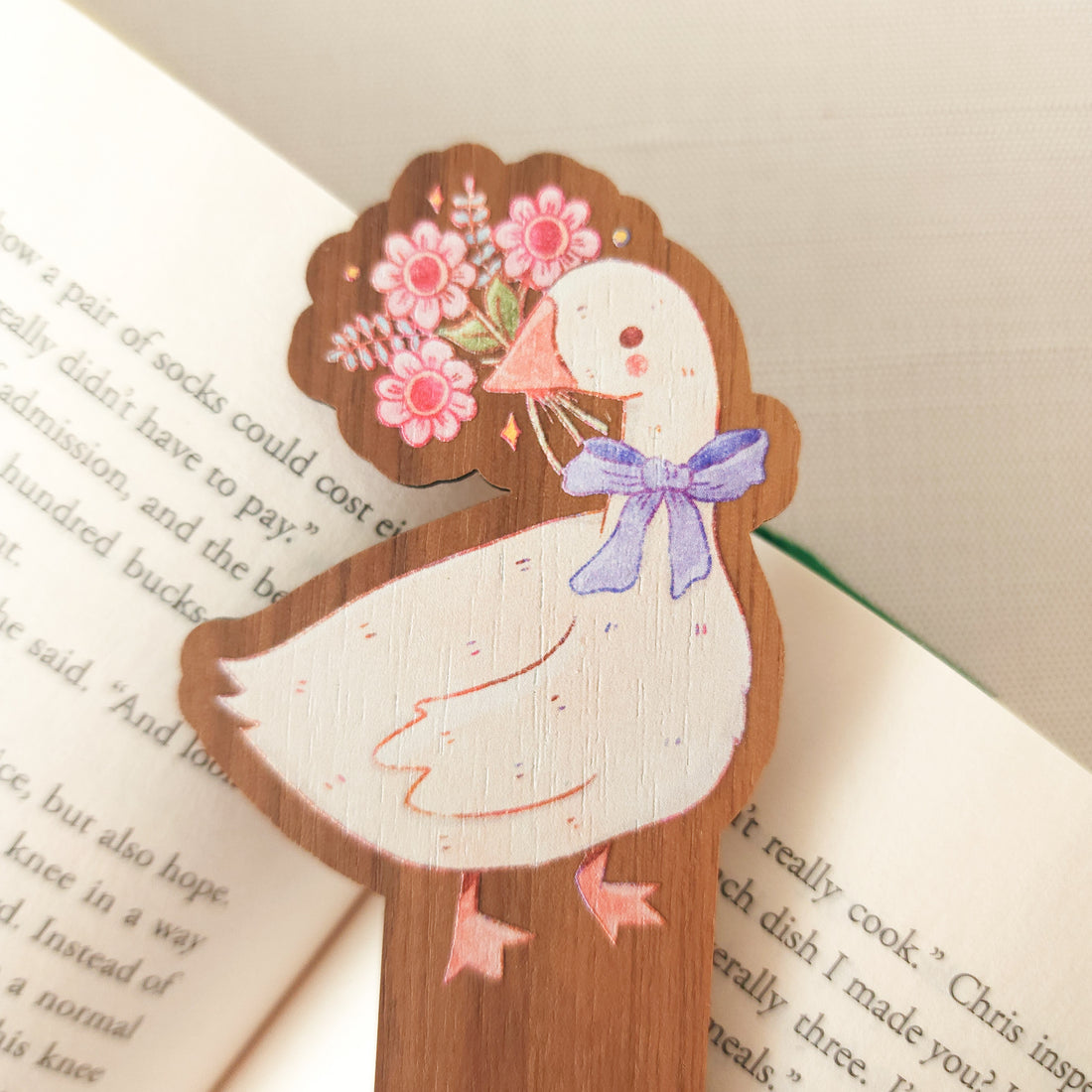 wooden bookmark with an illustration of a goose holding a bouquet sitting on an open book