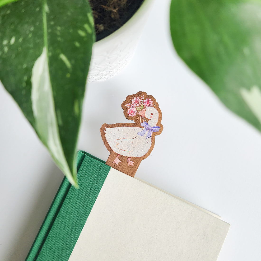 decorative goose bookmark inside of a book on a white background with leaves