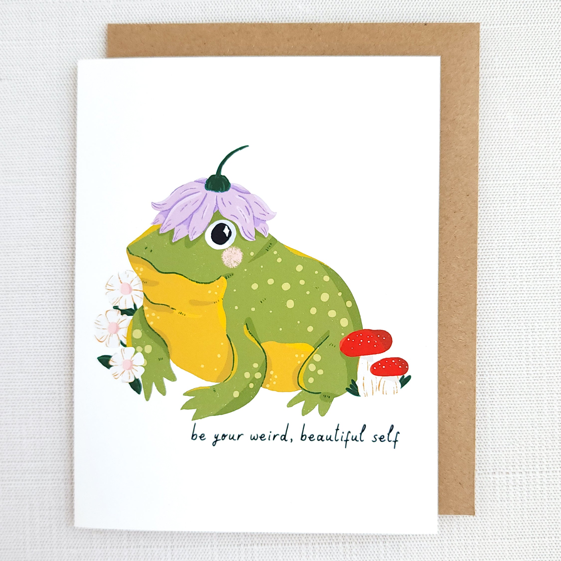Greeting card with a frog illustration and text be your weird beautiful self on a white background