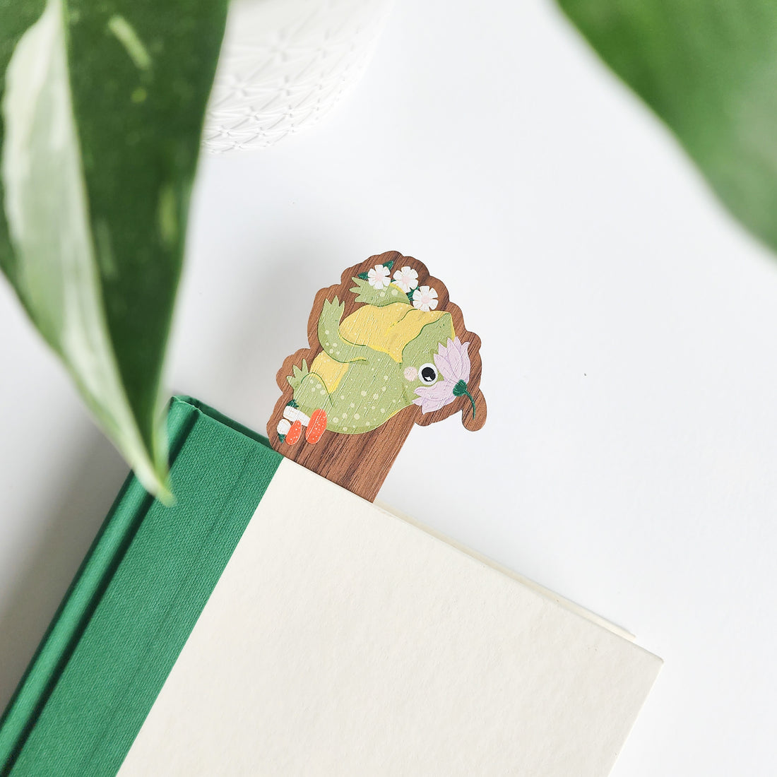 toad bookmark inside a green and white book on a white background with green leaves