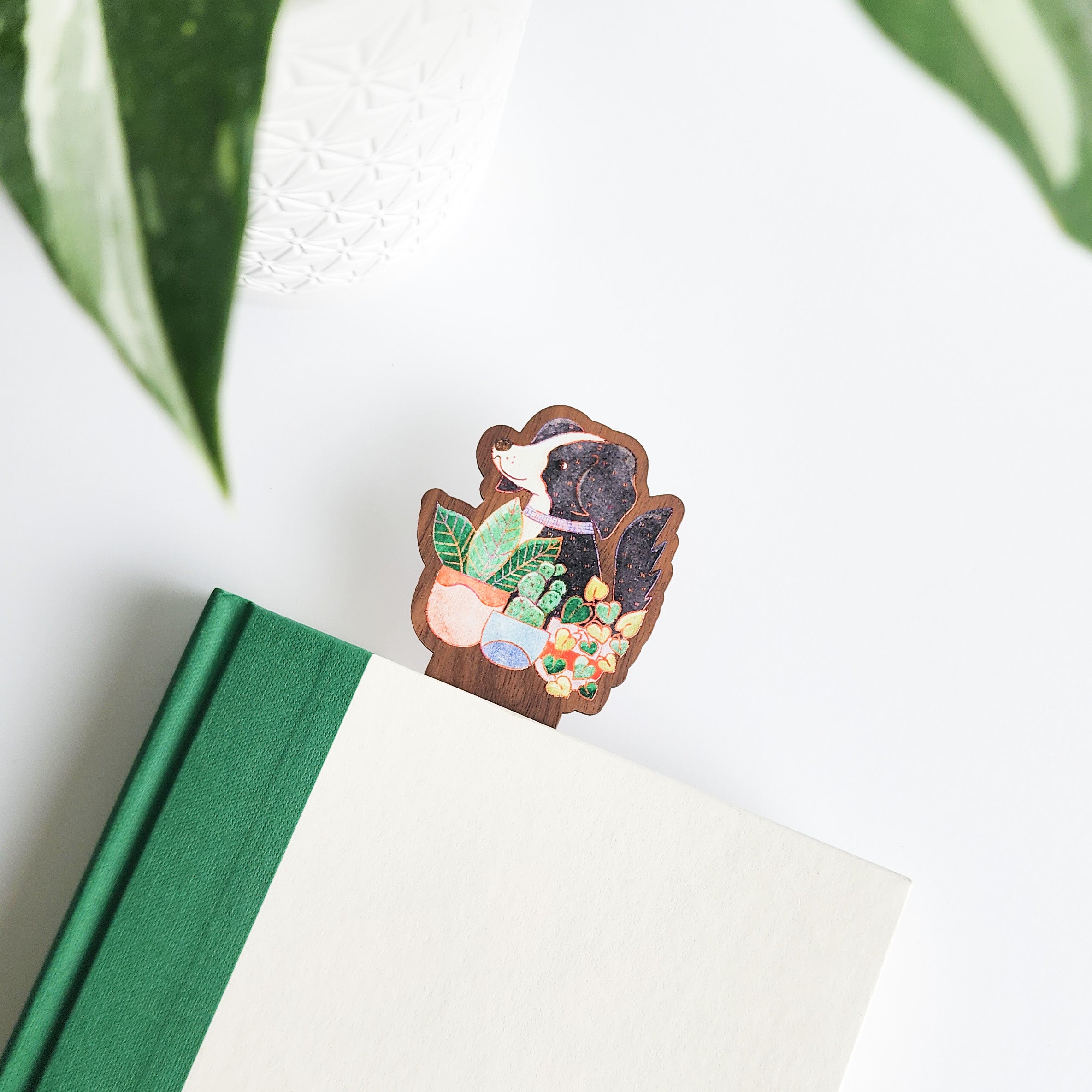 dog with houseplants bookmark inside a green and white book on a white background with leaves