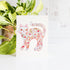 Decorative card with a floral cat design next to a potted plant on a white surface.