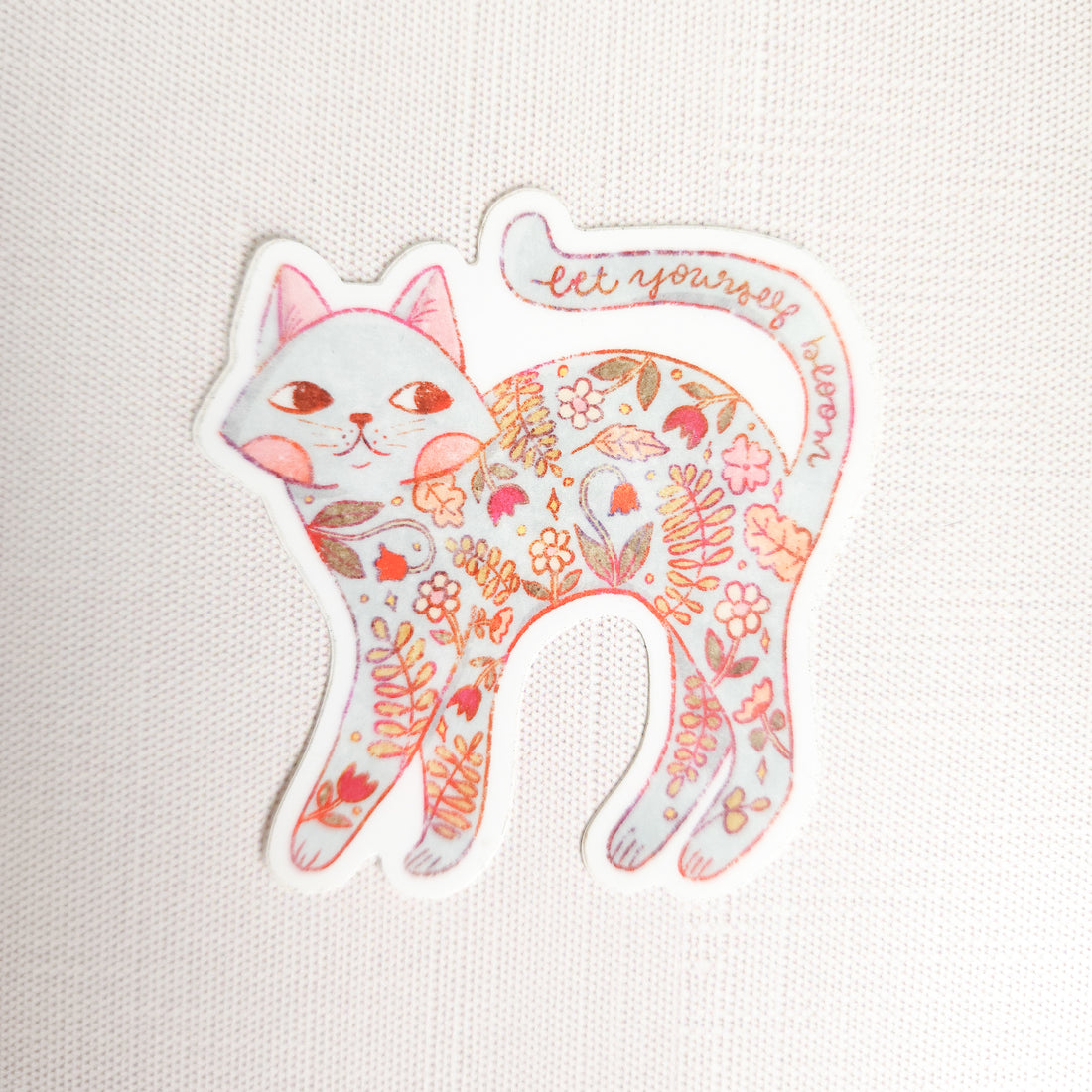 sticker of a floral cat with the words let yourself bloom on a linen background