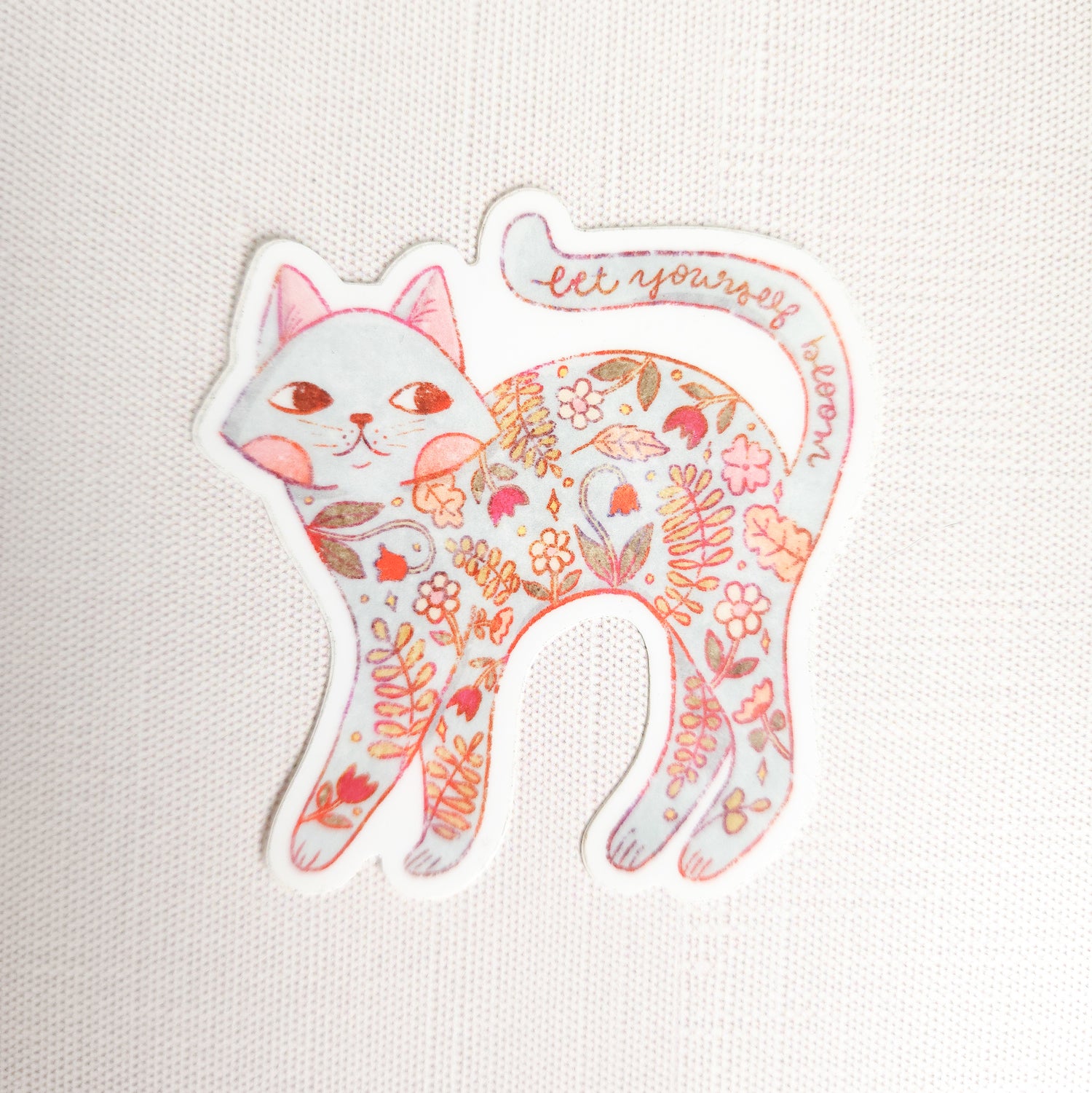 sticker of a floral cat with the words let yourself bloom on a linen background