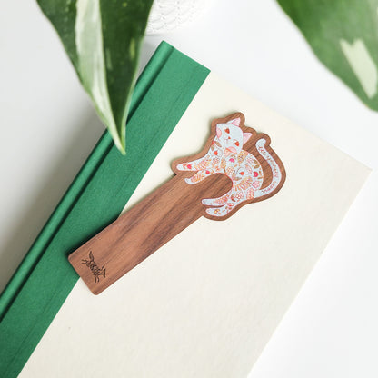 wooden bookmark with a floral cat design on a green and white book on a white background with leaves