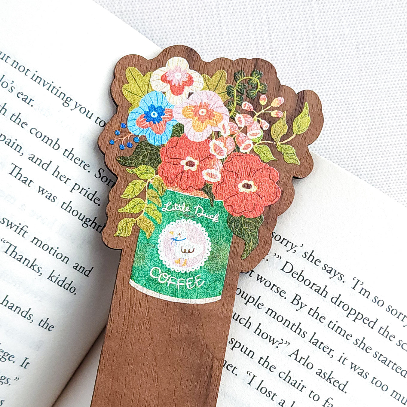 Walnut wood bookmark with a vintage-inspired Little Duck Coffee can filled with cheerful pink, yellow, and blue garden blooms sitting on an open book