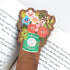 Walnut wood bookmark with a vintage-inspired Little Duck Coffee can filled with cheerful pink, yellow, and blue garden blooms sitting on an open book