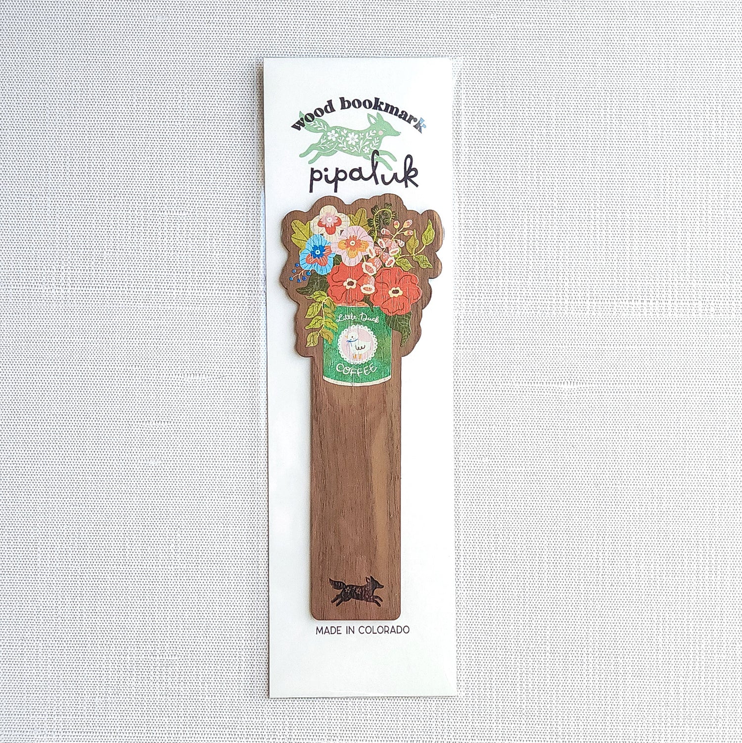 Walnut wood bookmark with a vintage-inspired Little Duck Coffee can filled with cheerful pink, yellow, and blue garden blooms in Pipaluk branded packaging on a neutral background