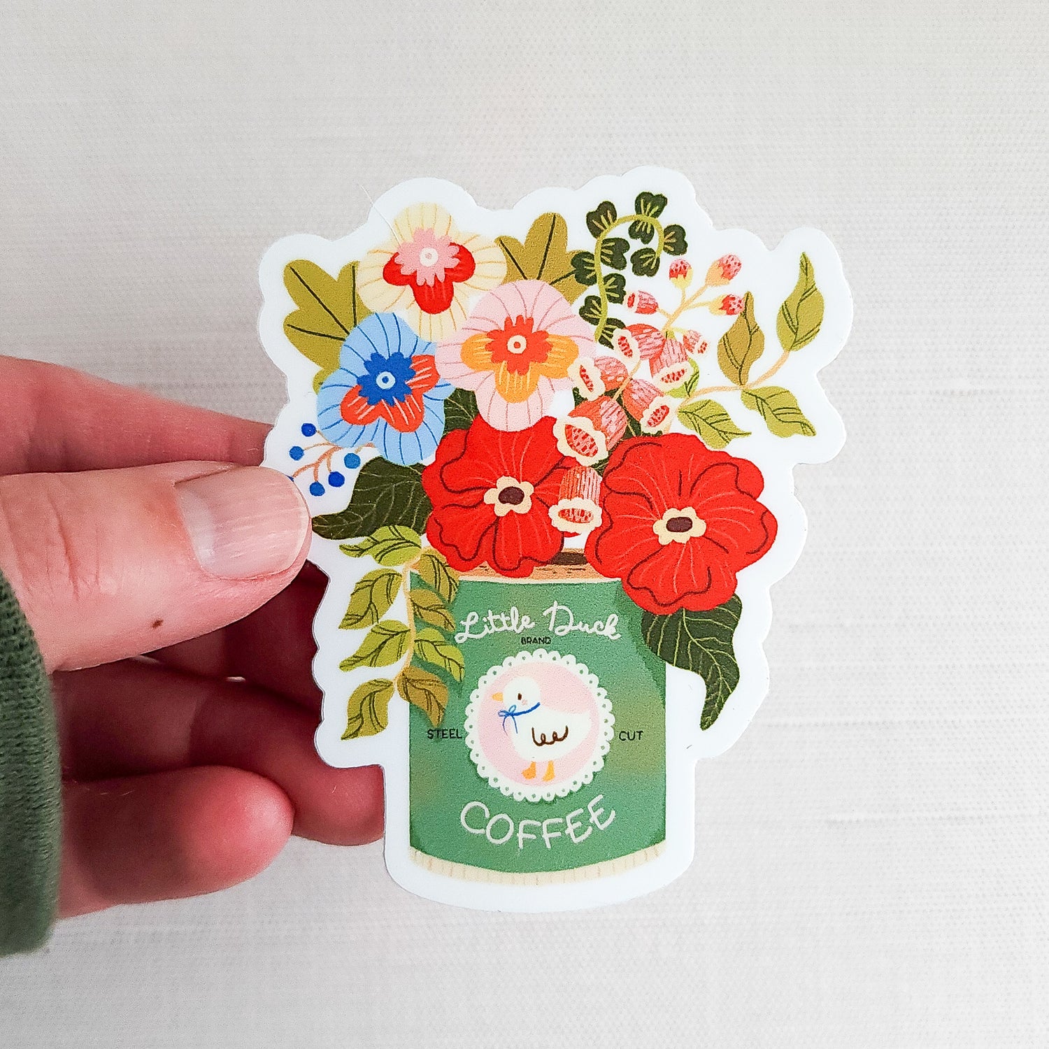 Waterproof vinyl sticker featuring an illustrated Little Duck Coffee can repurposed as a vase, filled with colorful garden flowers held in a hand on a neutral background