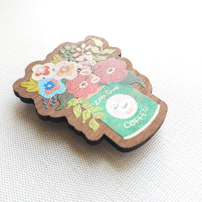 Wooden magnet with an illustrated Little Duck Coffee can repurposed as a vase, filled with cheerful pink, yellow, and blue flowers on a neutral background