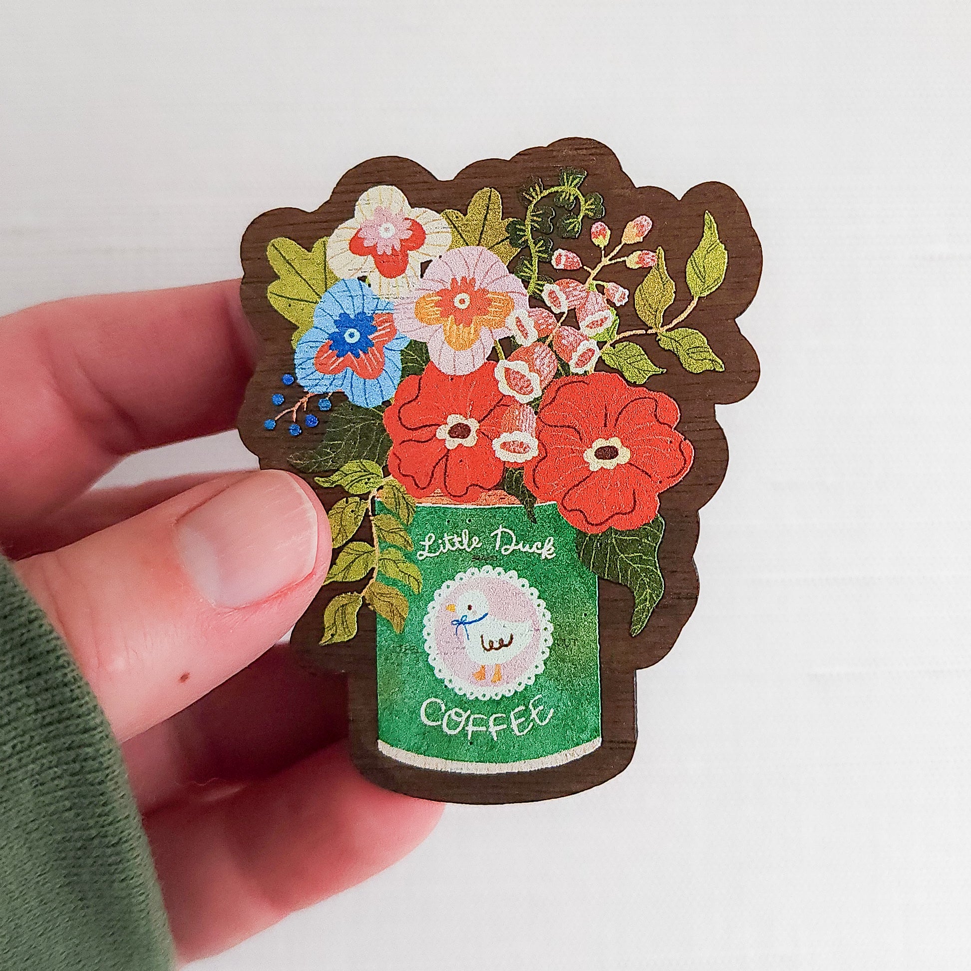 Wooden magnet with an illustrated Little Duck Coffee can repurposed as a vase, filled with cheerful pink, yellow, and blue flowers held in a hand