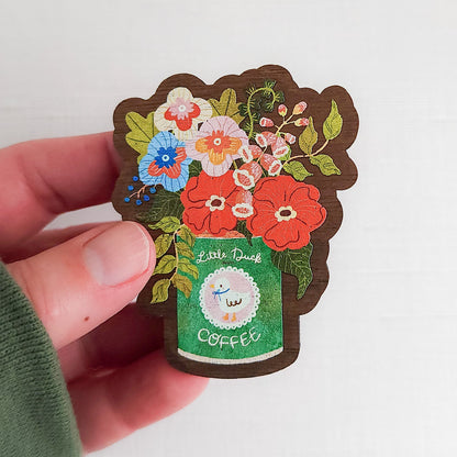 Wooden magnet with an illustrated Little Duck Coffee can repurposed as a vase, filled with cheerful pink, yellow, and blue flowers held in a hand