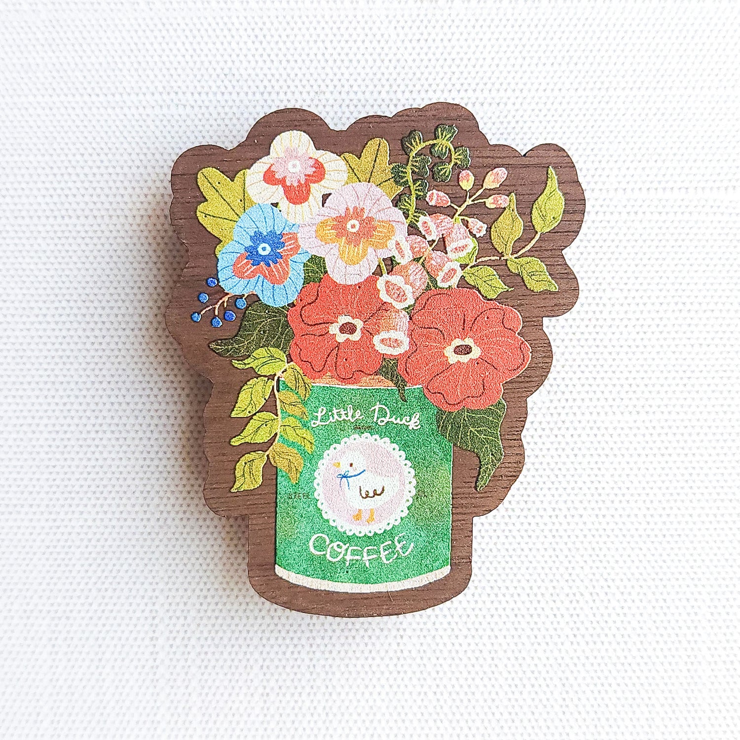 Wooden magnet with an illustrated Little Duck Coffee can repurposed as a vase, filled with cheerful pink, yellow, and blue flowers on a neutral background