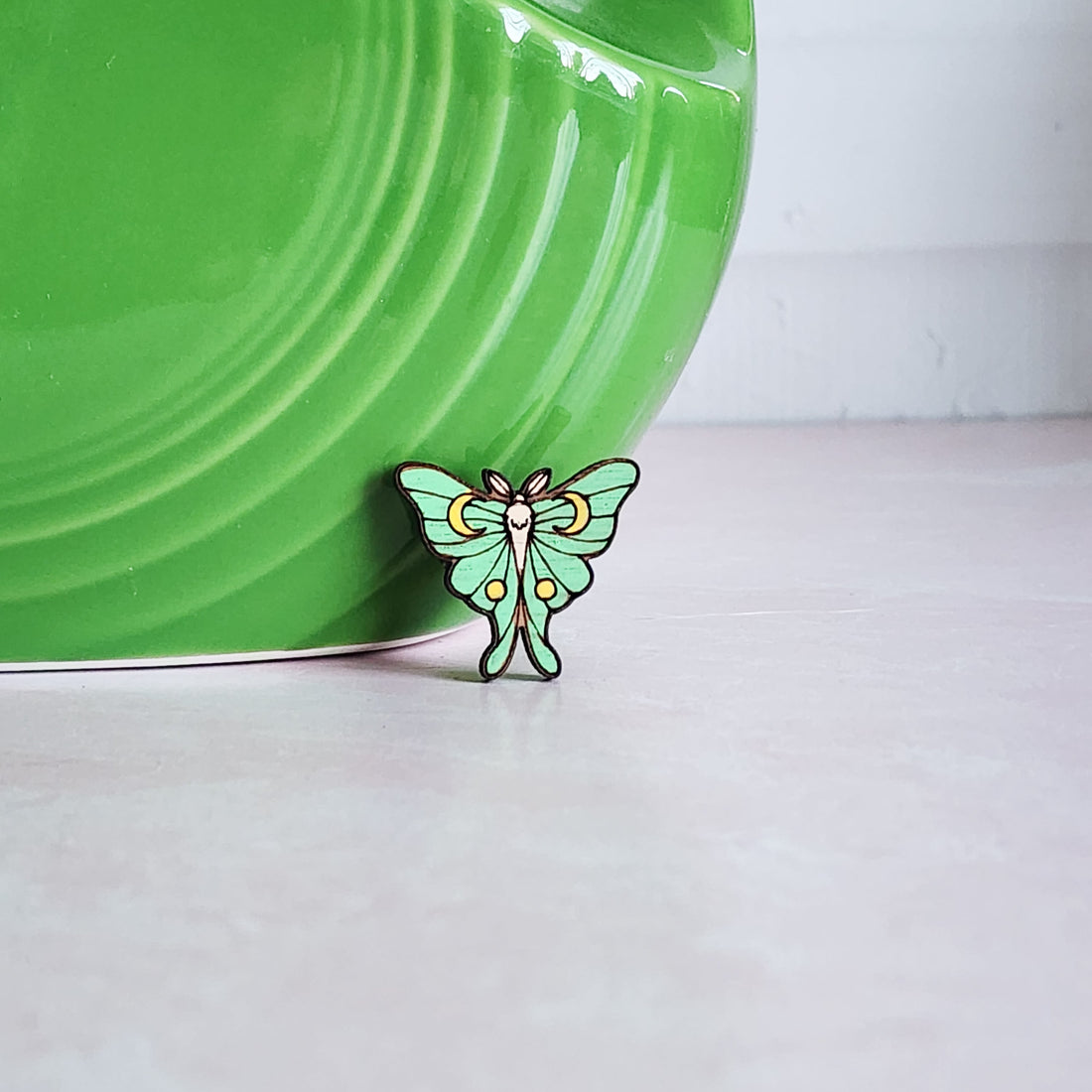 green luna moth pin with moons on the wings in front of a green vase