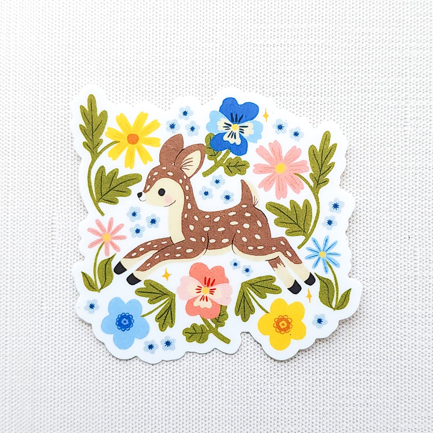 Vinyl sticker featuring a sweet spotted fawn dancing among colorful wildflowers, with pink, yellow, blue, and green floral details on a neutral background.