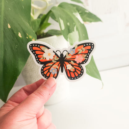 Butterfly-shaped sticker held by a hand with green leaves in the background