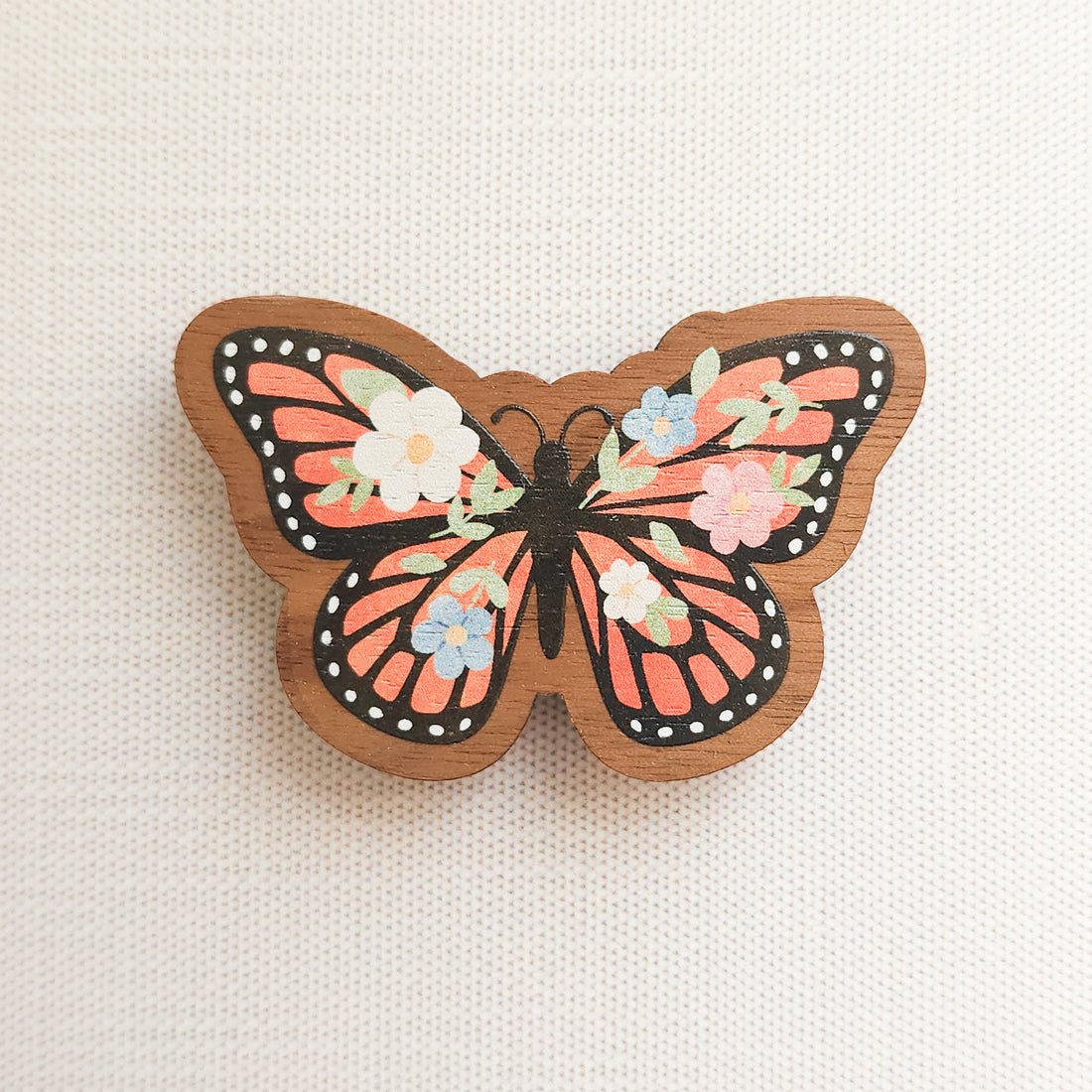 wooden magnet with an illustration of a monarch butterfly with flowers in its wings on a linen background