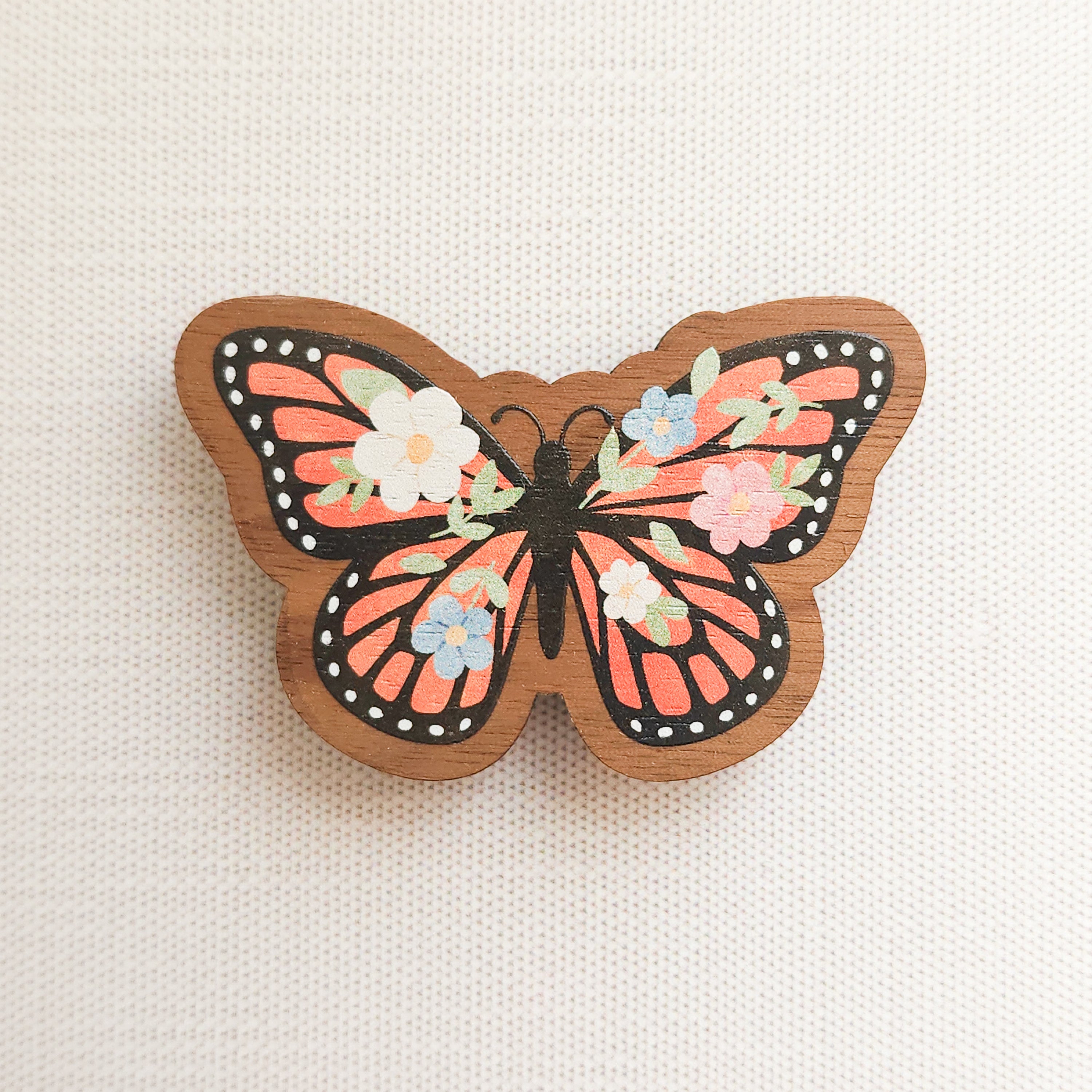wooden magnet with an illustration of a monarch butterfly with flowers in its wings on a linen background